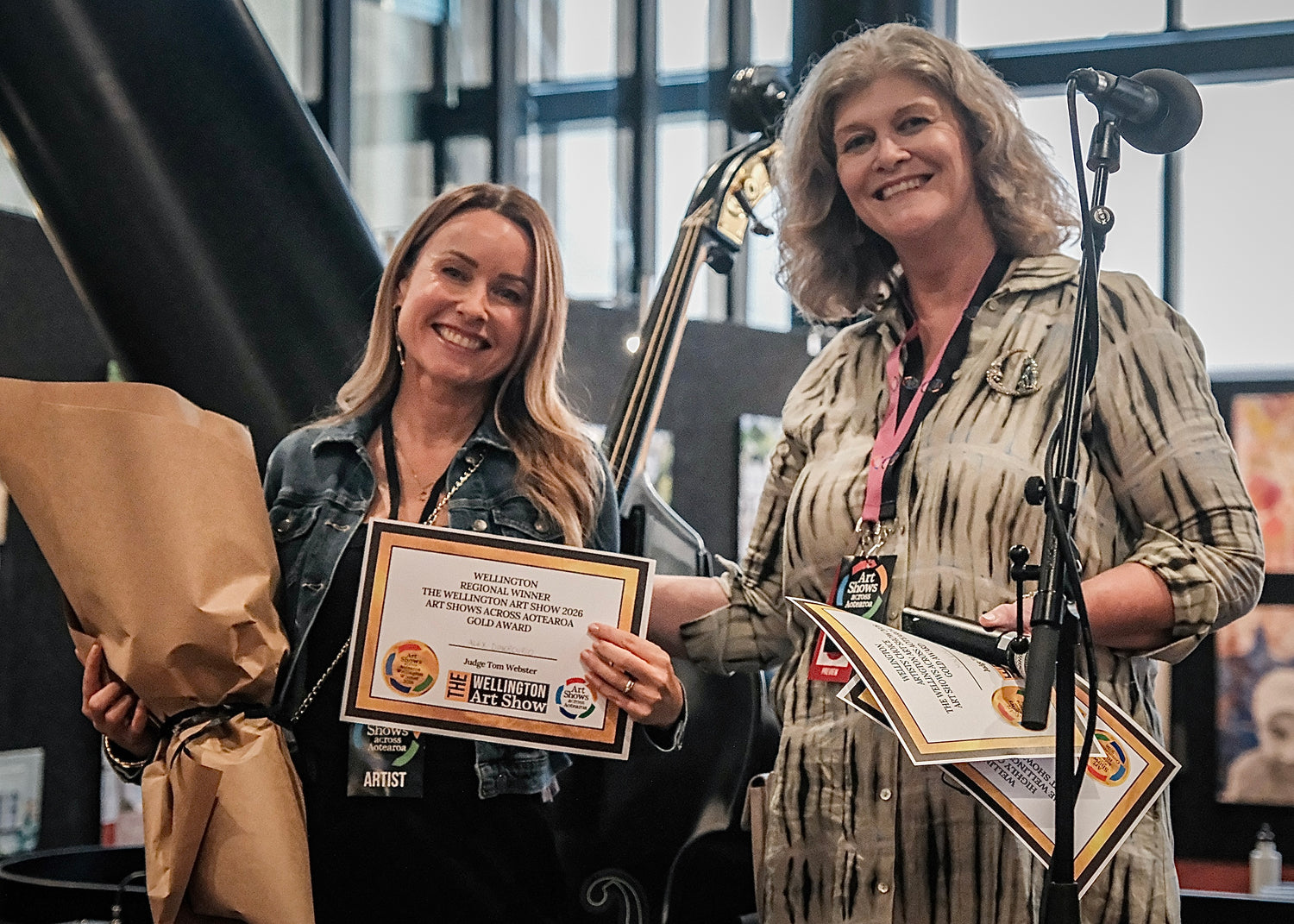 Artist Alex DiMercurio is accepting her Regional Gold Award prize from Wellington Art Shows director Kate Morrison on stage at the art show.