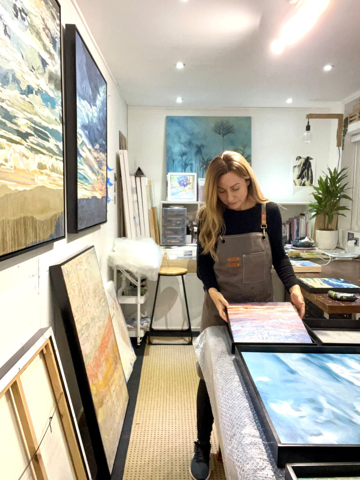 Alex DiMercurio preparing framed original paintings in her Wellington art studio