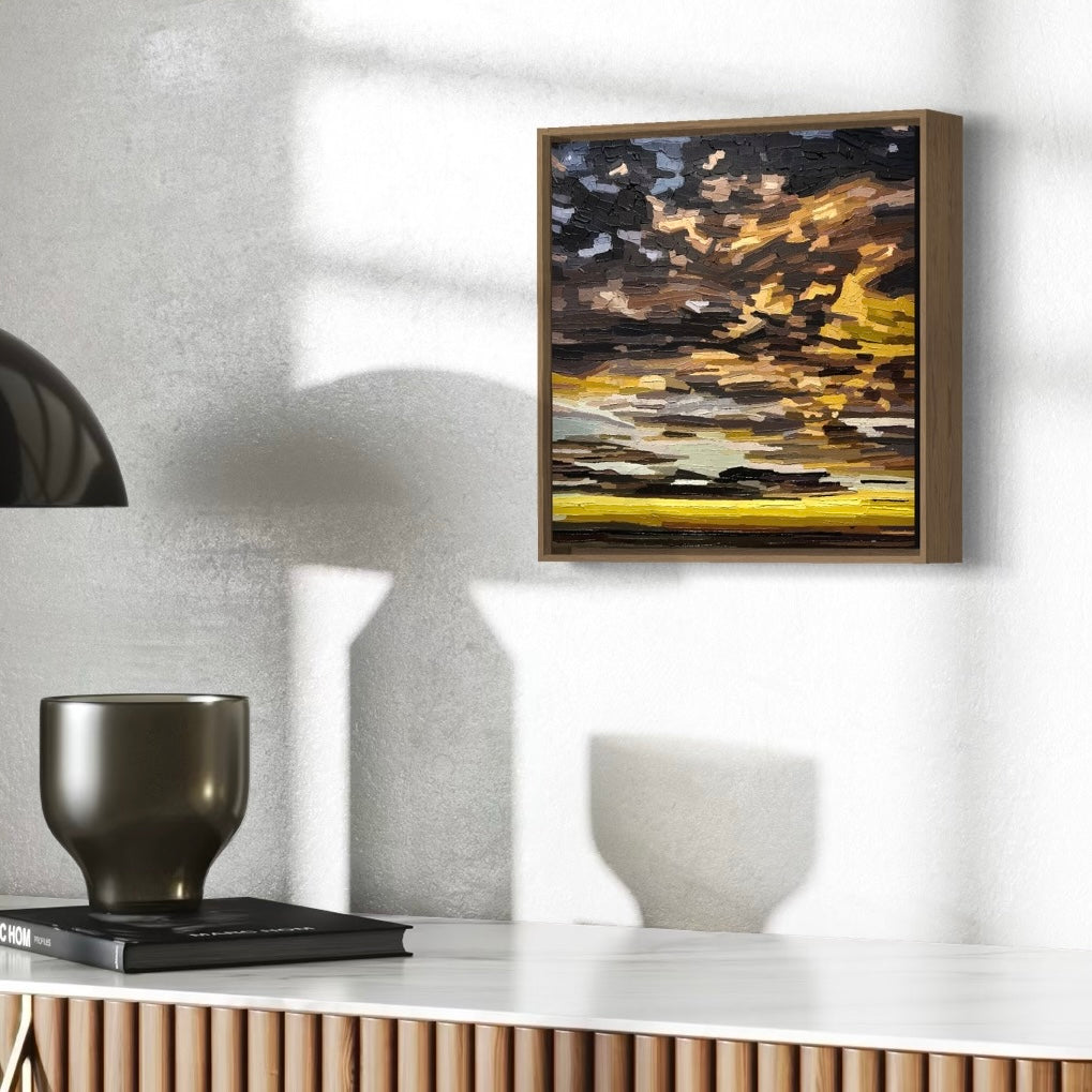 Abstract textural cloud painting with a mix of brown, black, and yellow colours. And some pale blue sky behind. Framed in wood.