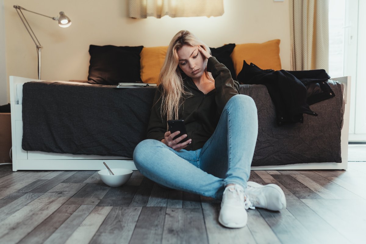 woman-sits-on-floor-and-looks-at-her-cell-phone